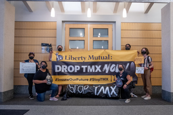 people stand in front of a banner urging liberty mutual to drop TMX