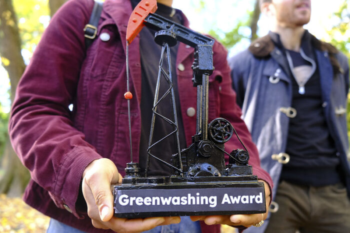 a person holding a miniature oil derrck with the plaque that reads "greenwashing award"