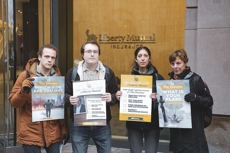 Activists stand outside Liberty Mutual's Boston headquarters with various signs featuring messages for the new CEO, Tim Sweeney