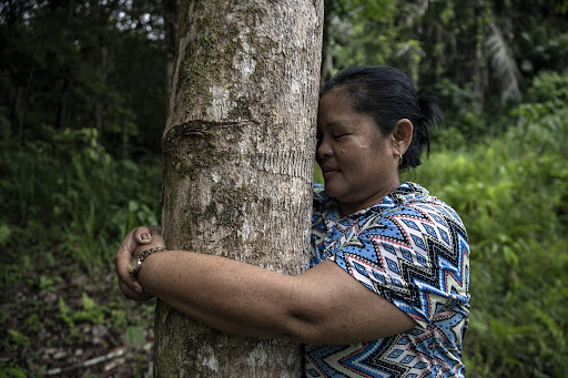 Long Isun community member (woman) hugging a tree as a symbol of gratitude towards mother nature