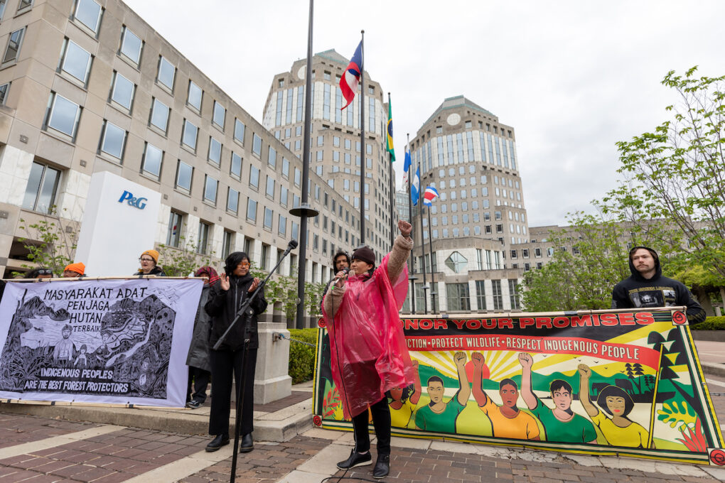 Delima Silalahi, recent Goldman Prize honoree, delivers a speech outside P&G headquarters in Cincinnati with individuals holding banners behind her that read "Indigenous peoples are the best forest protectors" and "Protect wildlife, respect Indigenous people."