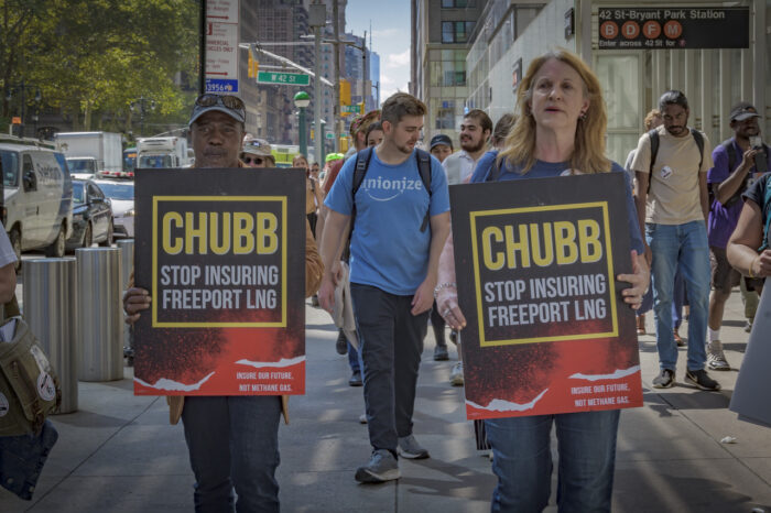 Melanie and Manning marching to Chubb's office in NYC, holding signs that say "Chubb: Stop insuring Freeport LNG. Insure our future, not methane gas." Behind them is a crowd of activists.