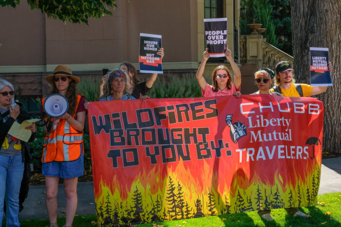 Seven activits gathered outside the Insurance Leadership Forum holding a banner that reads "Wildfires brought to you by: Chubb, Liberty, Mutual, Travelers" that depicts trees on fire. Some people are holding smaller signs that include: "people over profit" "insure our future, not methane gas" and "liberty mutual insures methane"